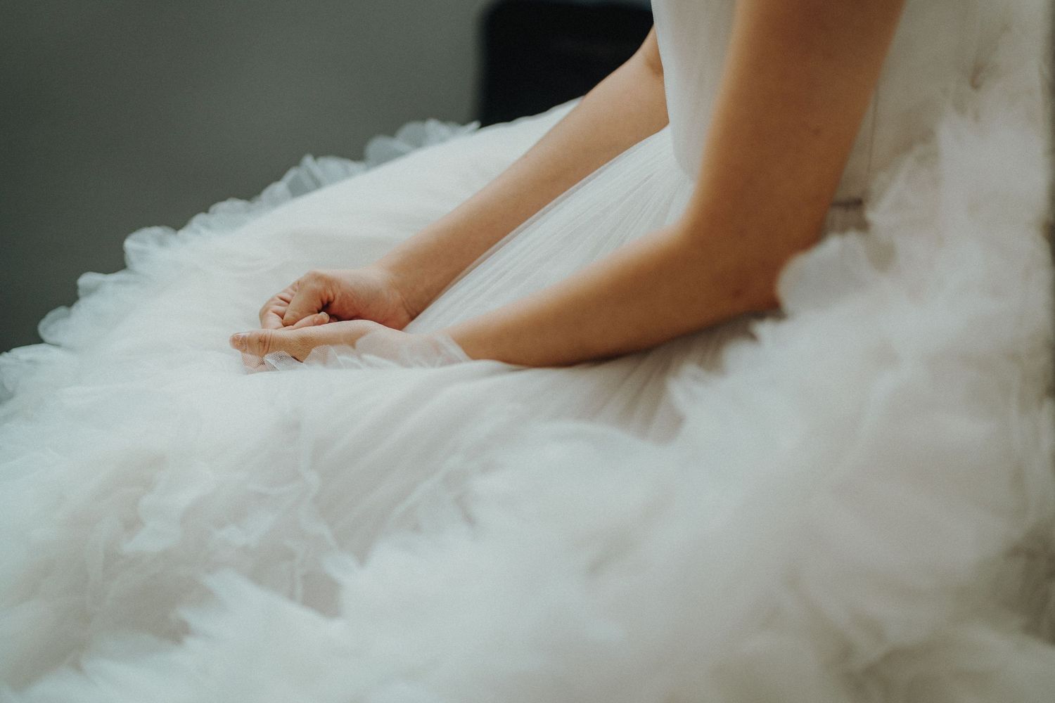 Close-up detail of hands resting on white tulle wedding dress fabric.