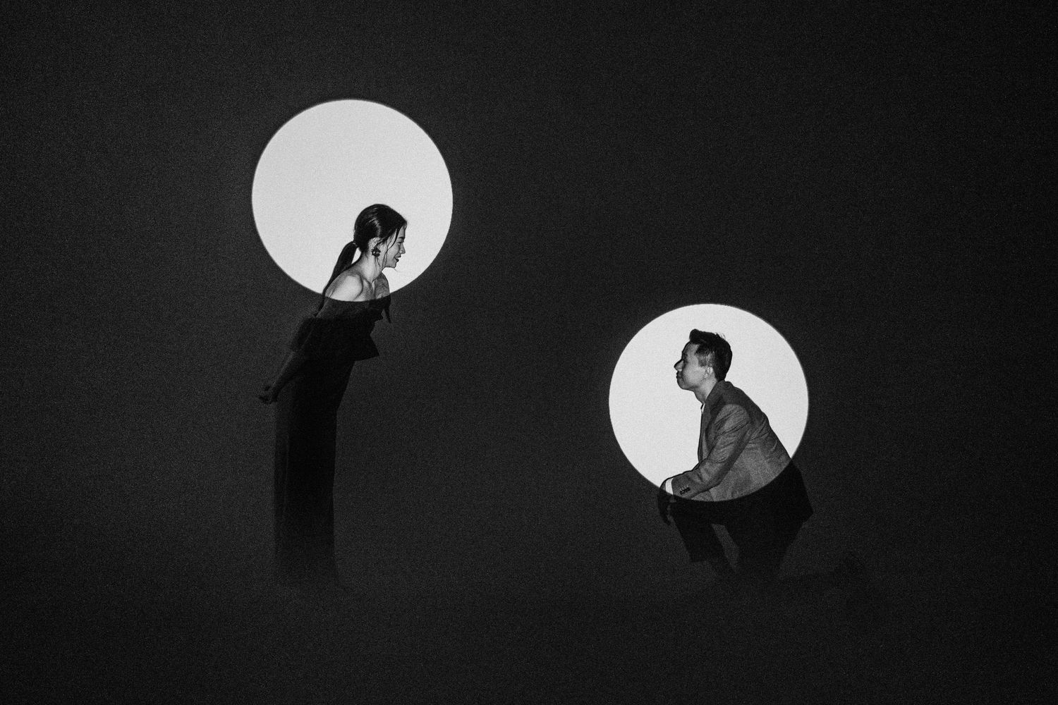 Two silhouetted figures in circular white spaces against a dark background creating a minimalist artistic composition.