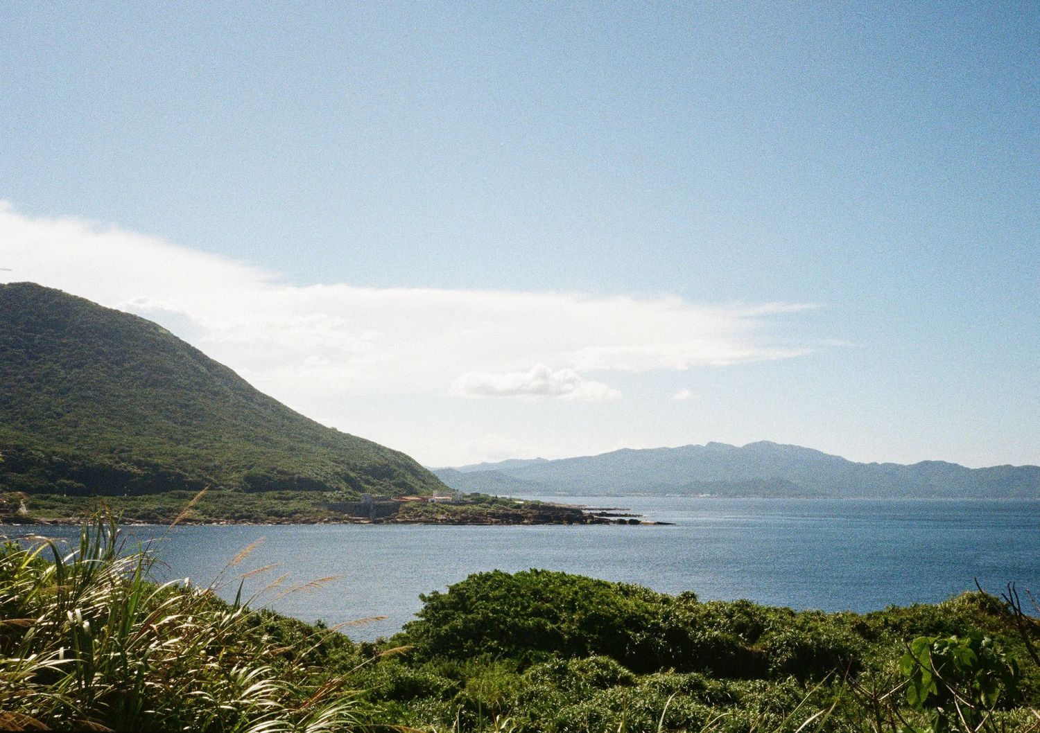 Panoramic coastal view of mountains meeting the ocean under a bright blue sky.