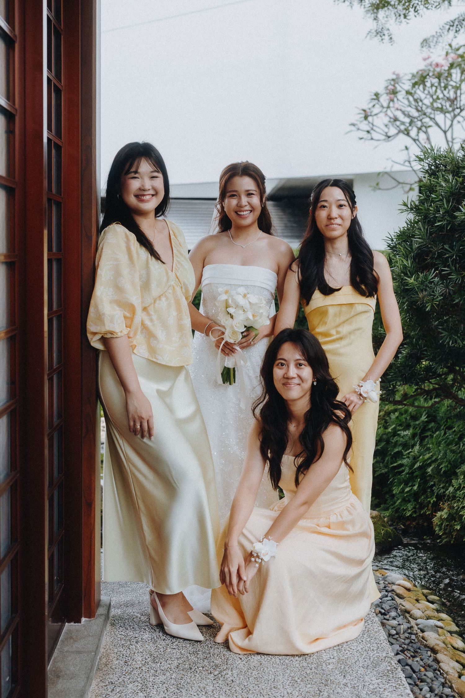 Bridesmaids wearing soft pastel yellow dresses gather together for a wedding photo outdoors.