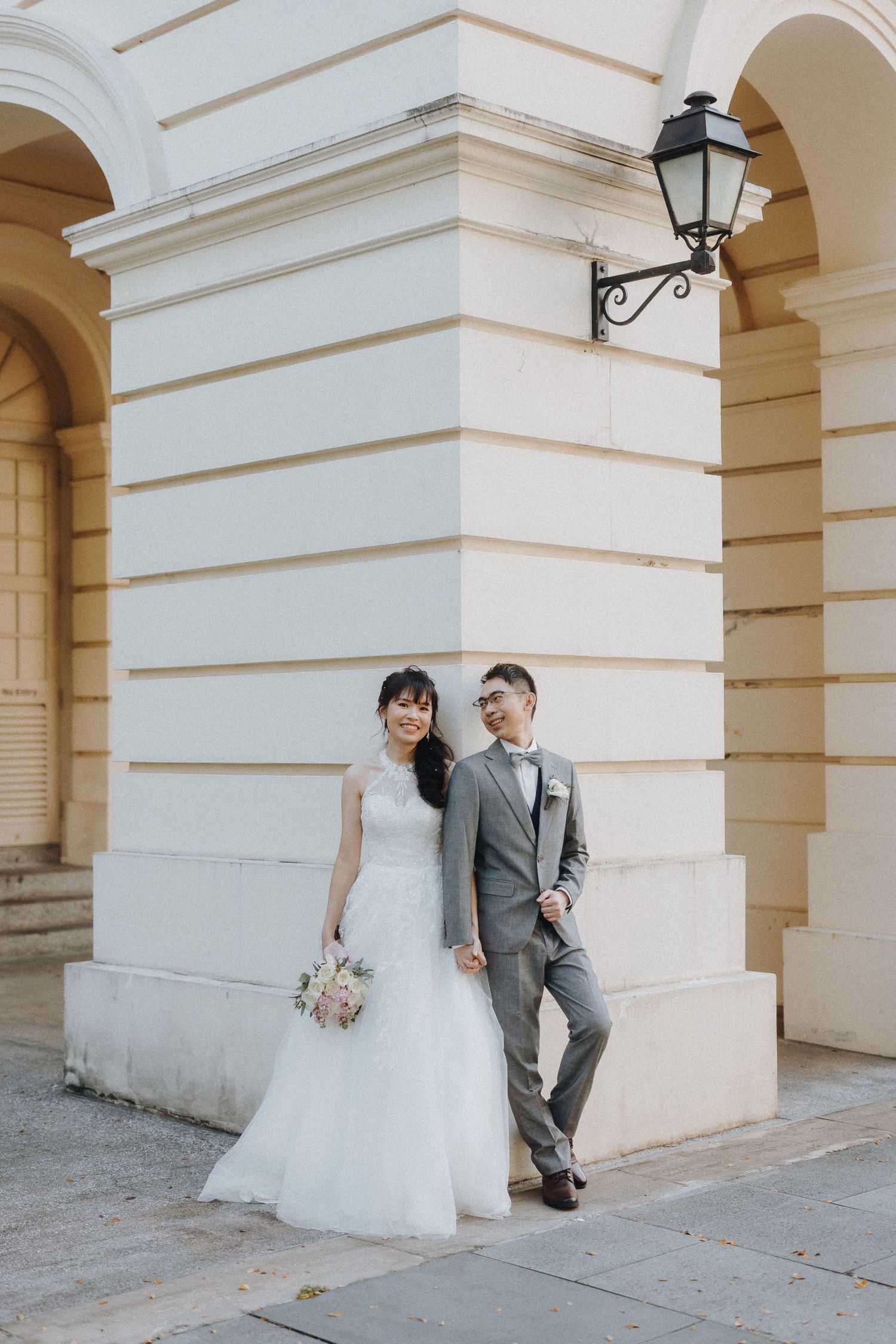 Wedding couple poses playfully behind stone pillars of elegant building with classic architecture.