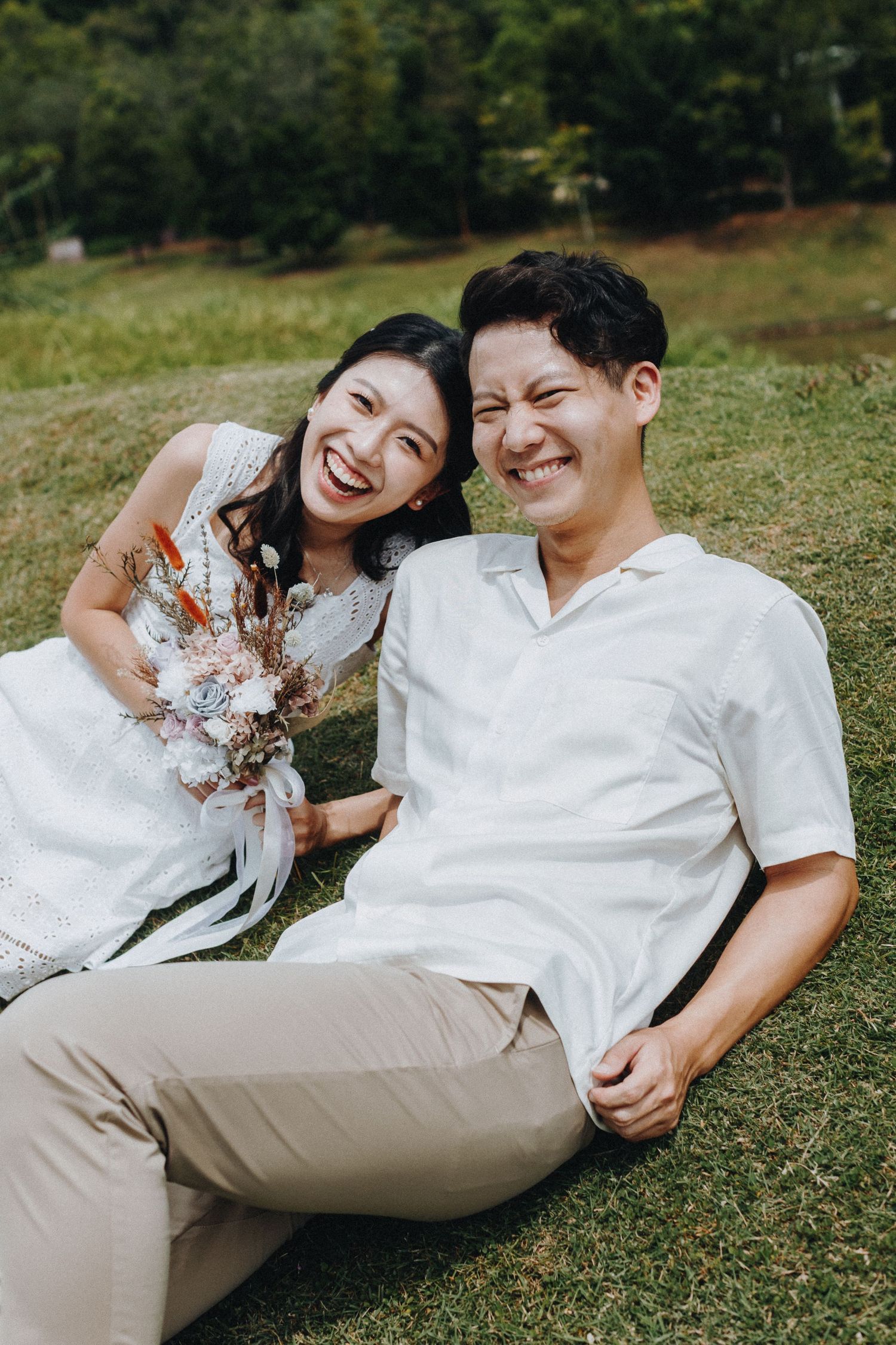 Happy couple sitting on grass sharing joyful moment with flowers and natural surroundings.