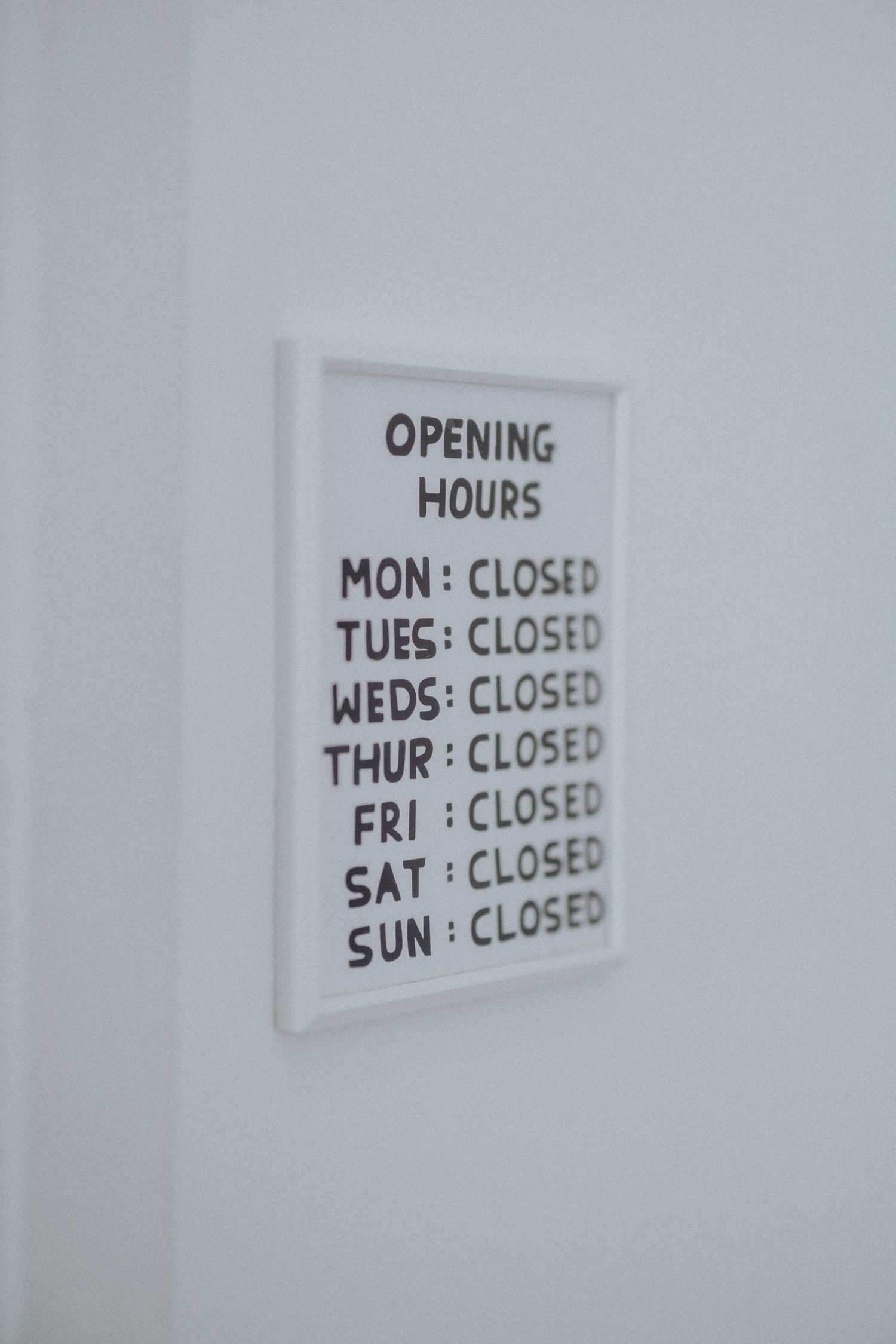 Business hours sign showing all days as closed mounted on white wall.