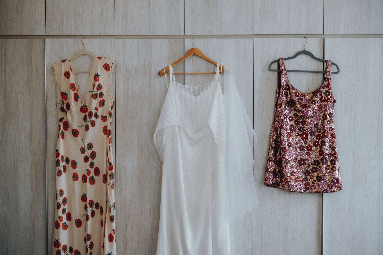 Three dresses hanging on a wall - floral print, white, and burgundy designs.