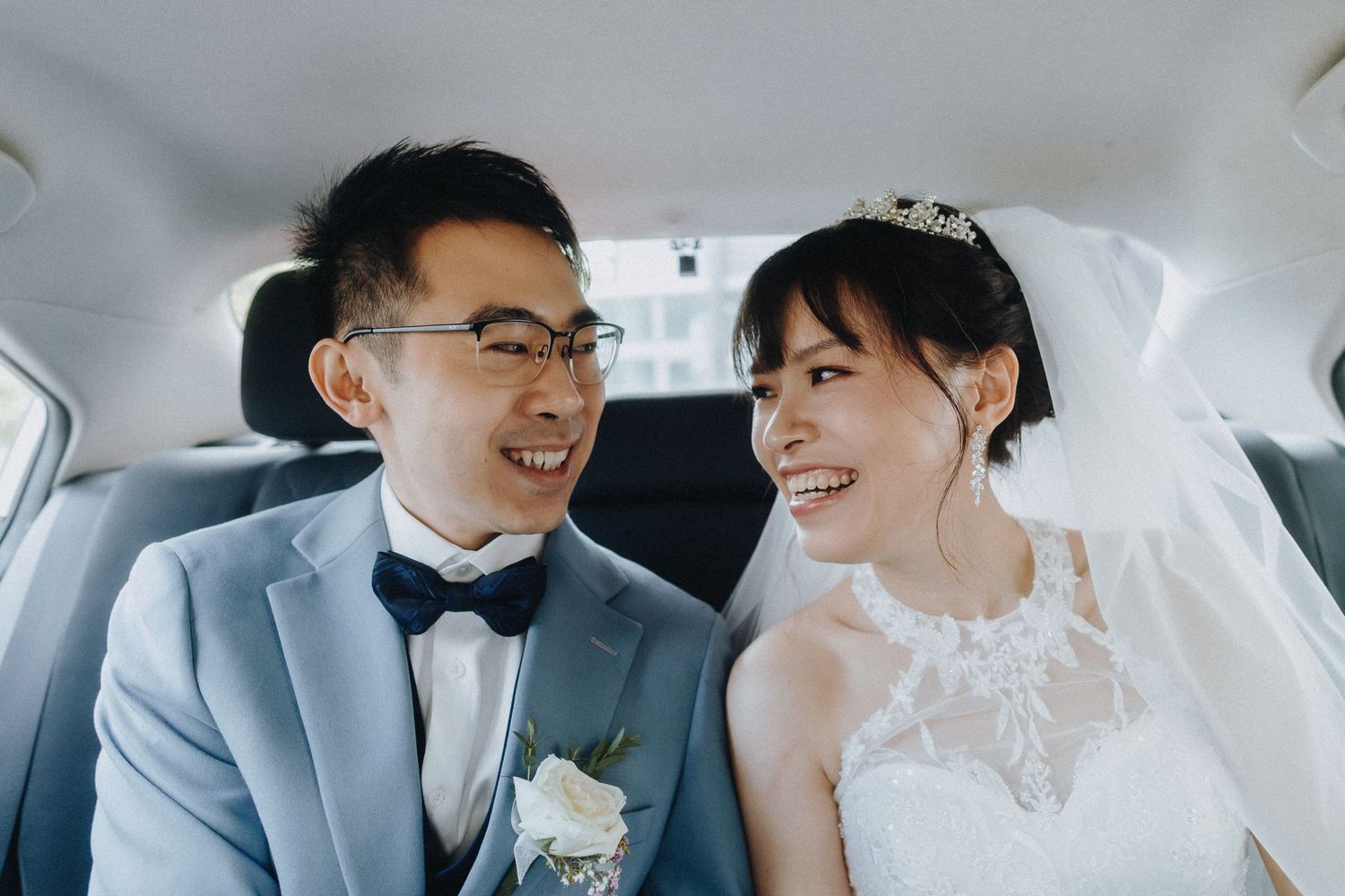 A joyful bride and groom share a candid moment while sitting in the backseat of a car.