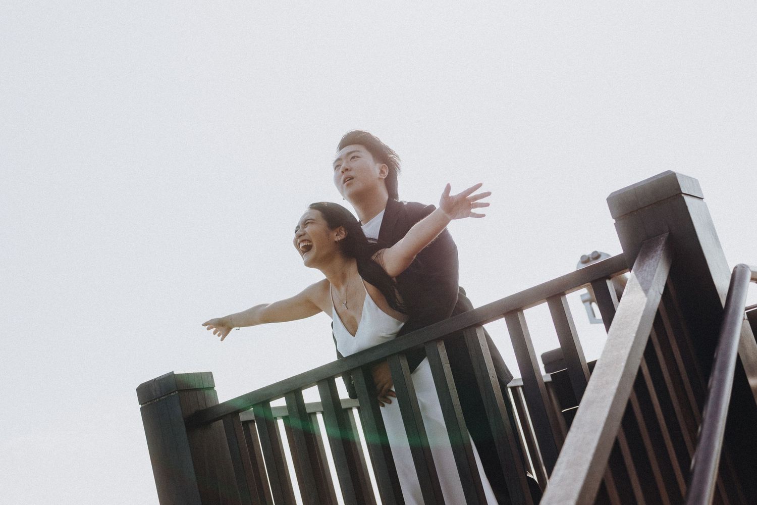 People leaning over railing of an elevated viewing platform against cloudy sky.