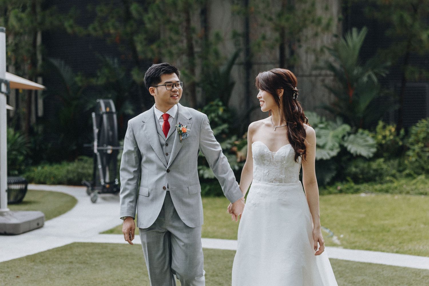 A couple in wedding attire walks along a garden path surrounded by lush greenery on their special day.