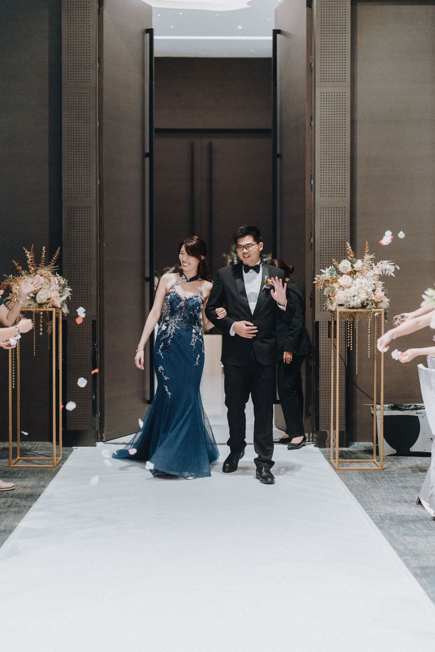 Wedding party in formal attire performs choreographed moves on an elegant white stage.