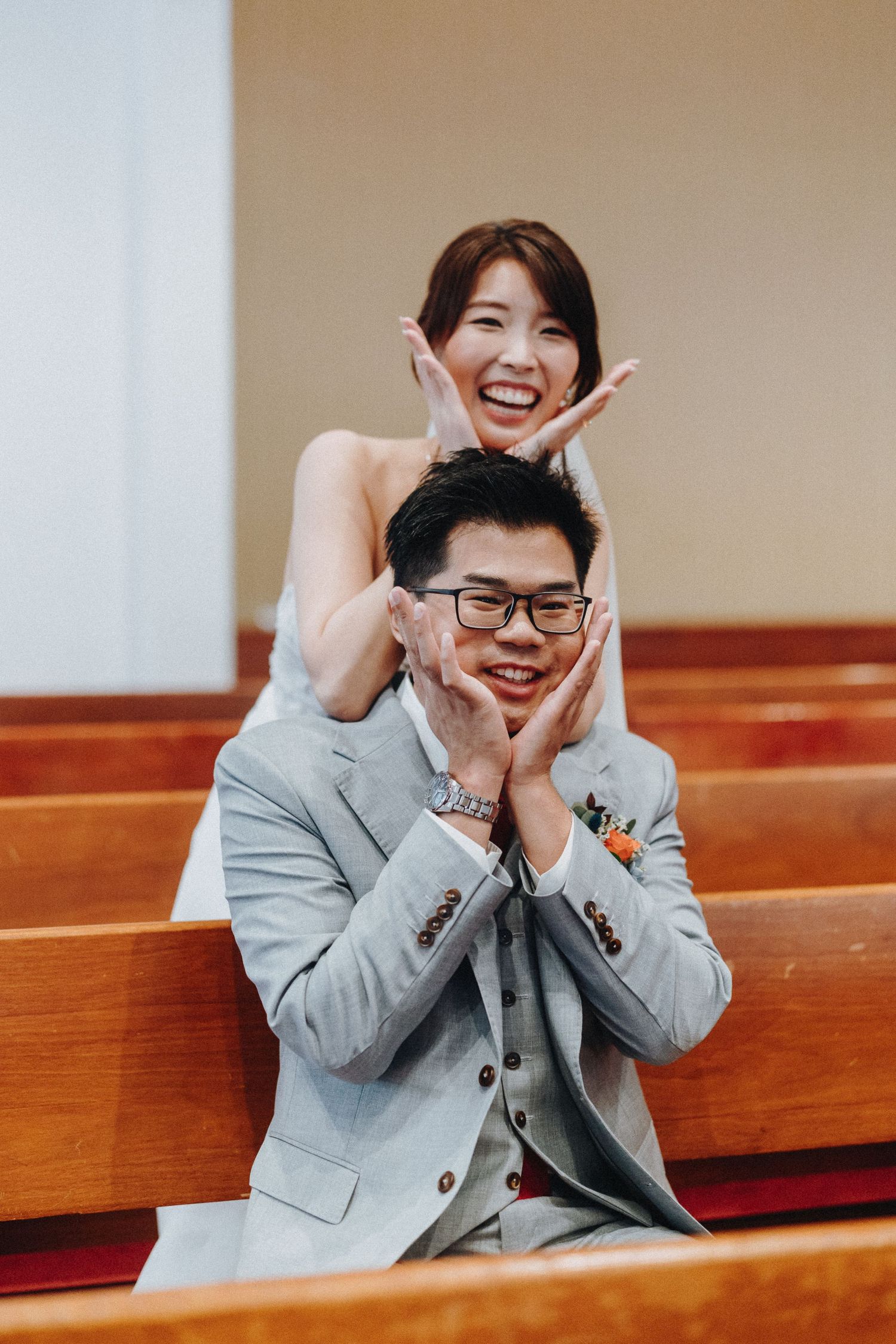 A joyful couple playfully poses in church pews during their wedding photoshoot.