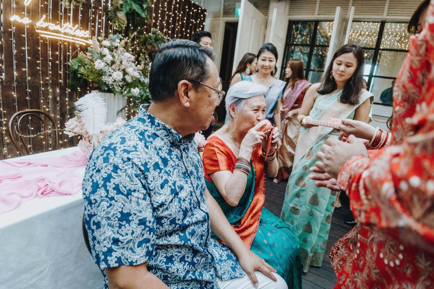 Elderly guests share an emotional moment at an Asian wedding reception with fairy lights and floral decor.