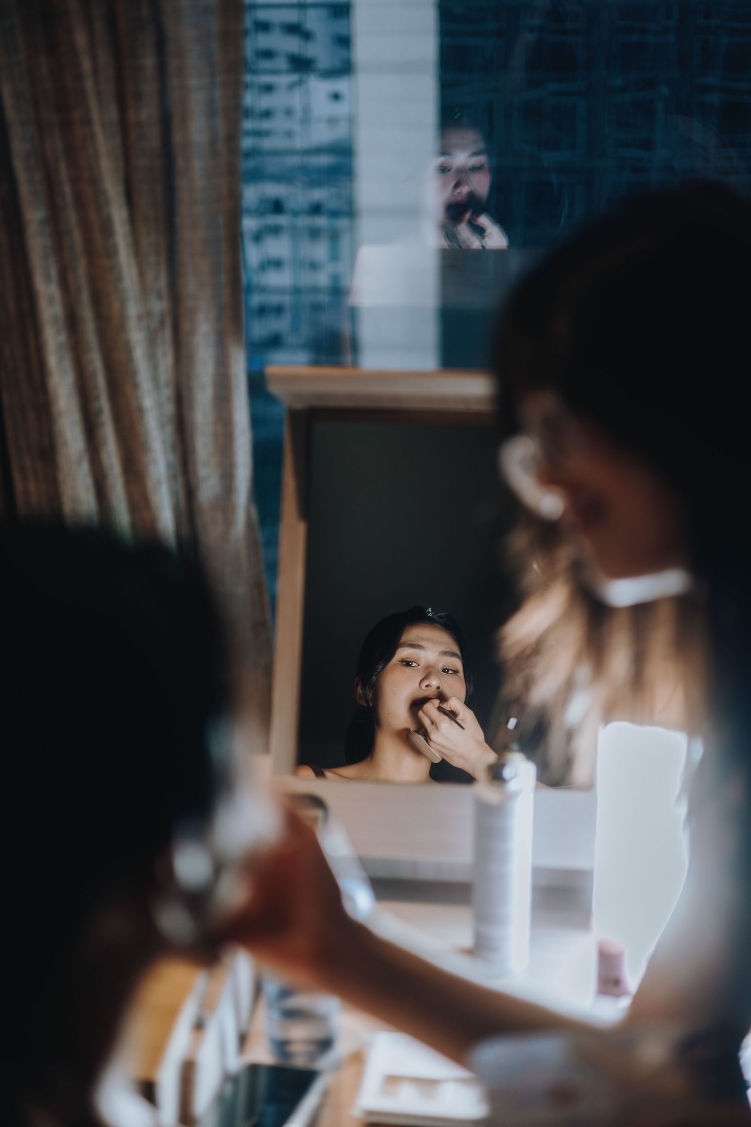 Bride applying lipstick while looking into a vanity mirror during wedding preparations.