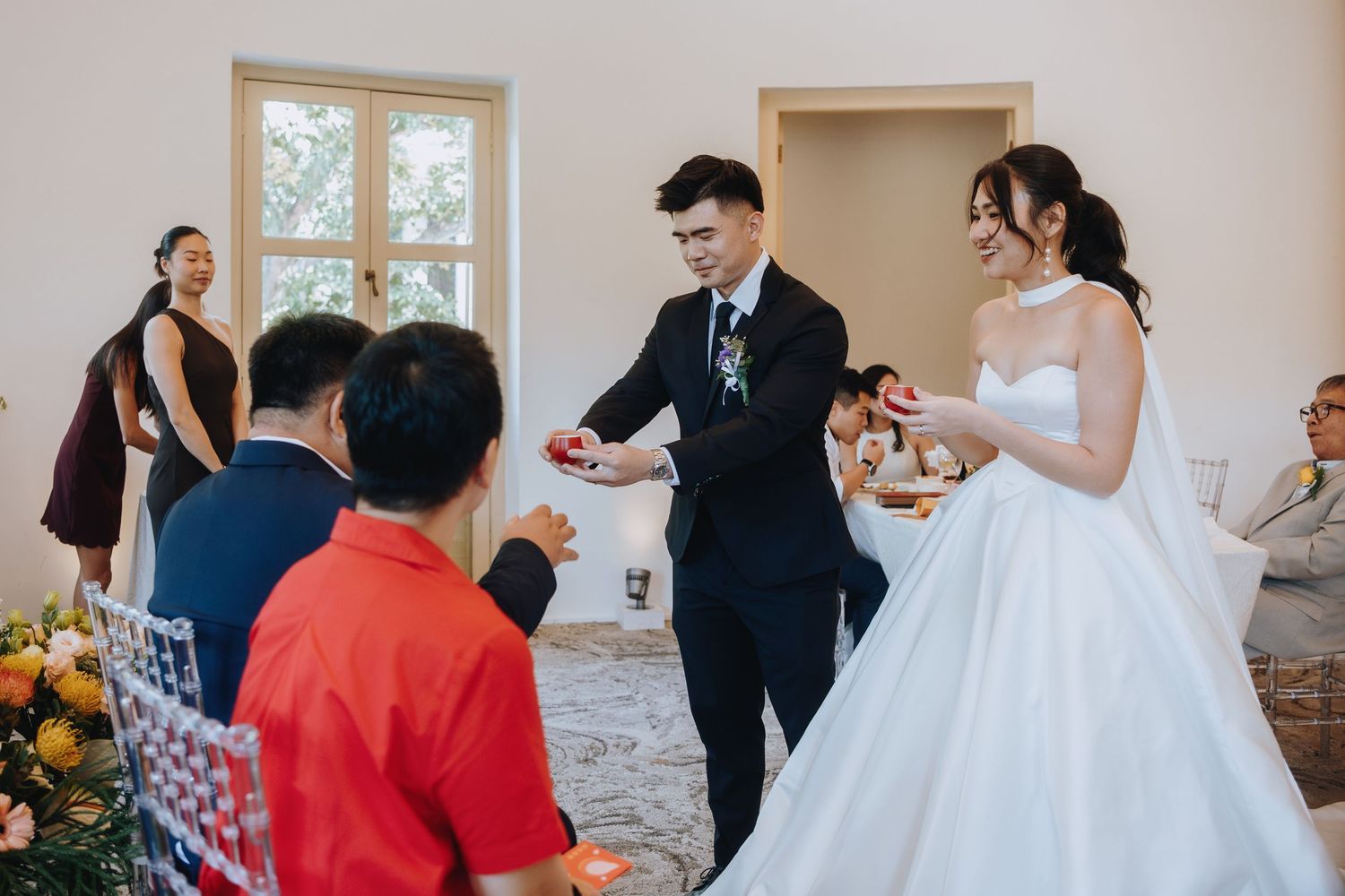 Groom presents bride with wedding rings during intimate indoor ceremony with guests watching.
