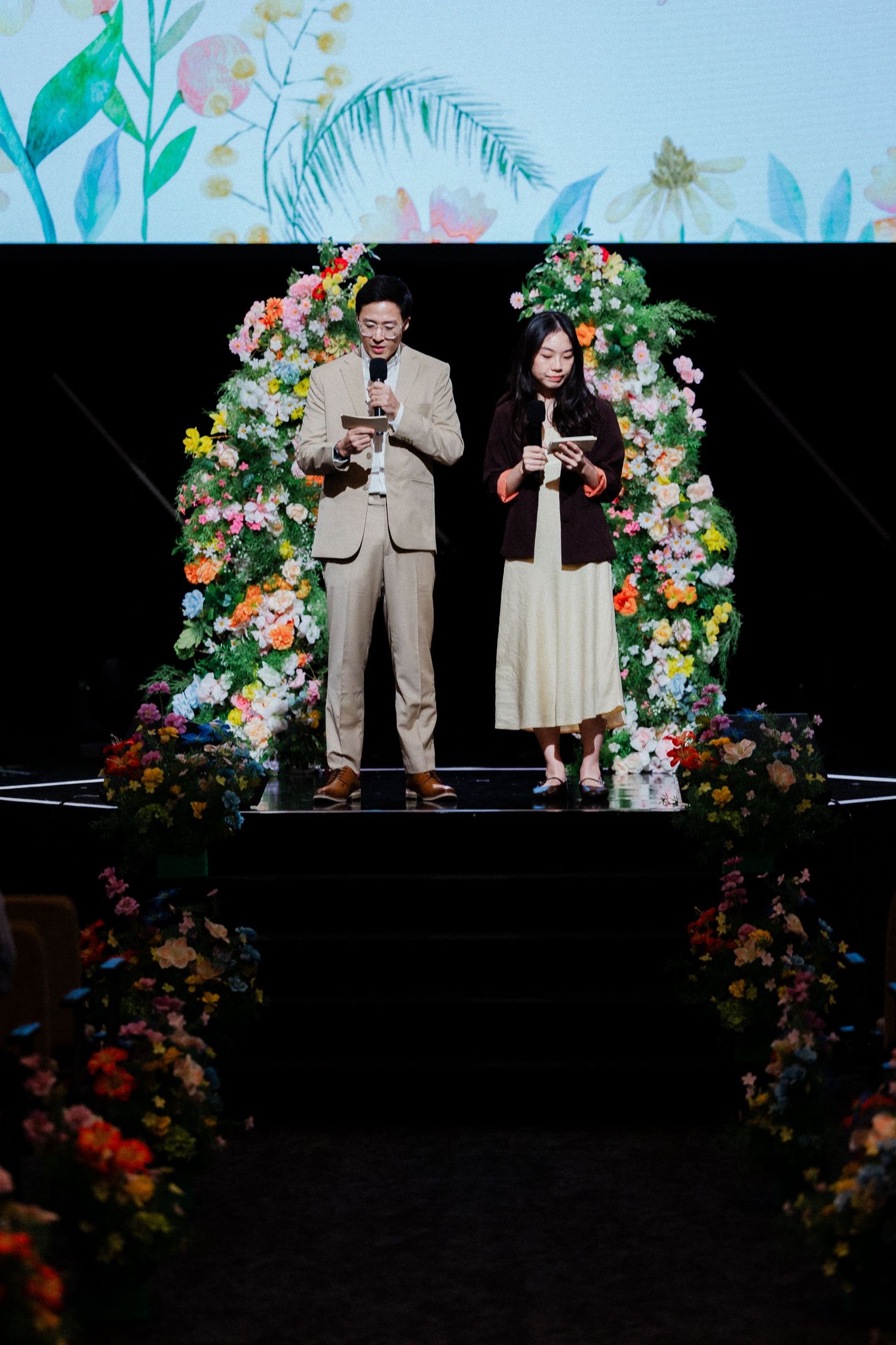 Couple exchanges vows on a floral arch-decorated stage during an elegant wedding ceremony.