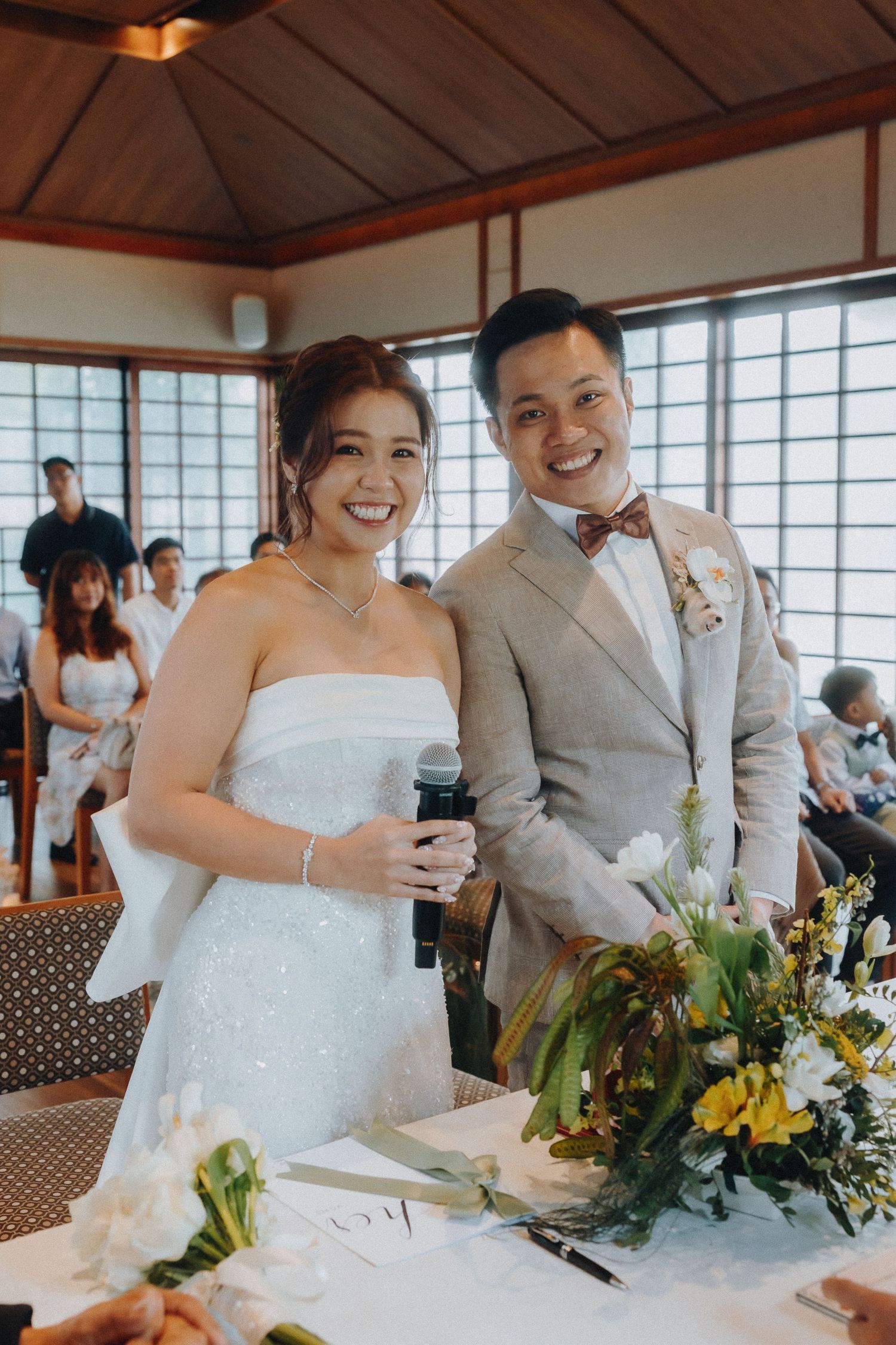 Wedding celebration inside traditional Asian venue with large windows and wooden ceiling.