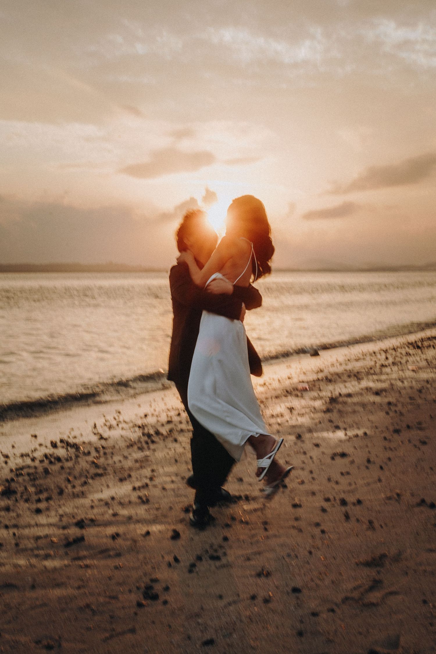 Silhouettes of couple dancing on beach with dramatic sunset lighting behind them.