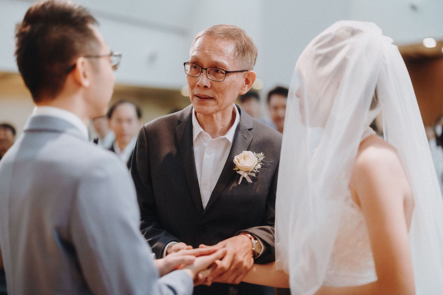 At a wedding ceremony, three figures interact and gesture while deep in conversation, with warm lighting and elegant decor.