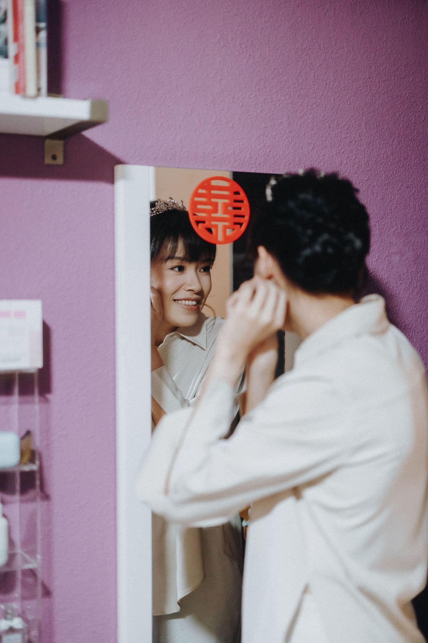 Wedding couple sharing a sweet moment during a traditional double happiness ceremony against a purple wall background.