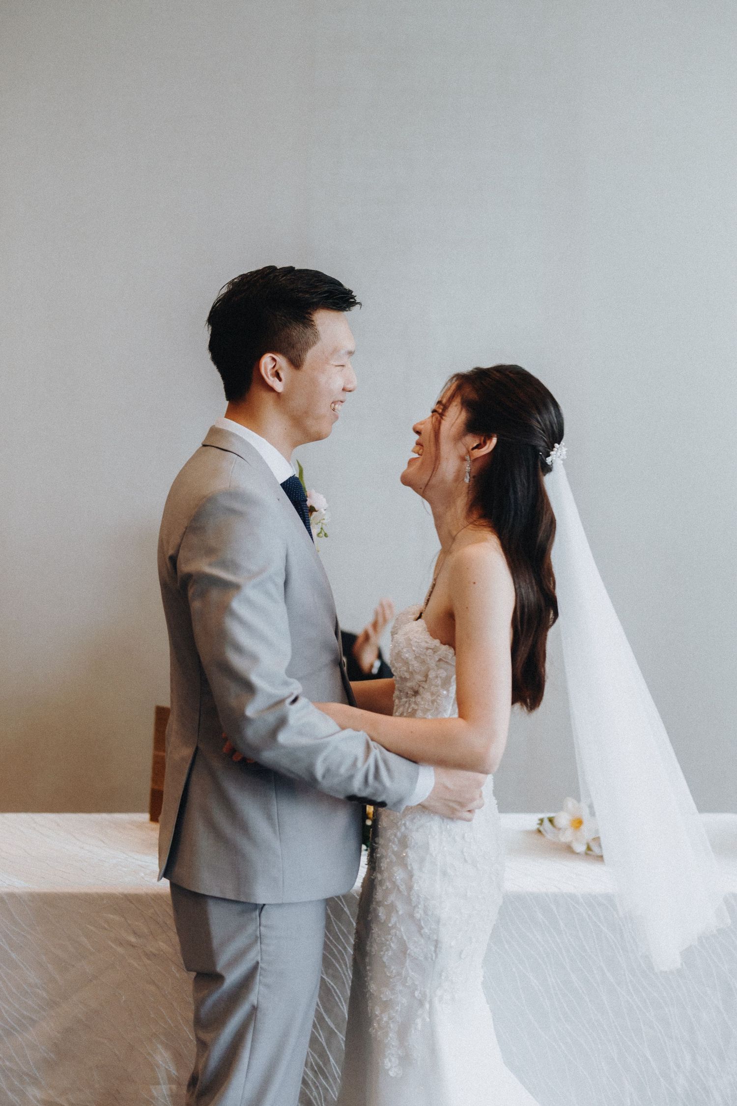 A series of intimate first look wedding photos showing a couple in a grey suit and white dress against a light wall.