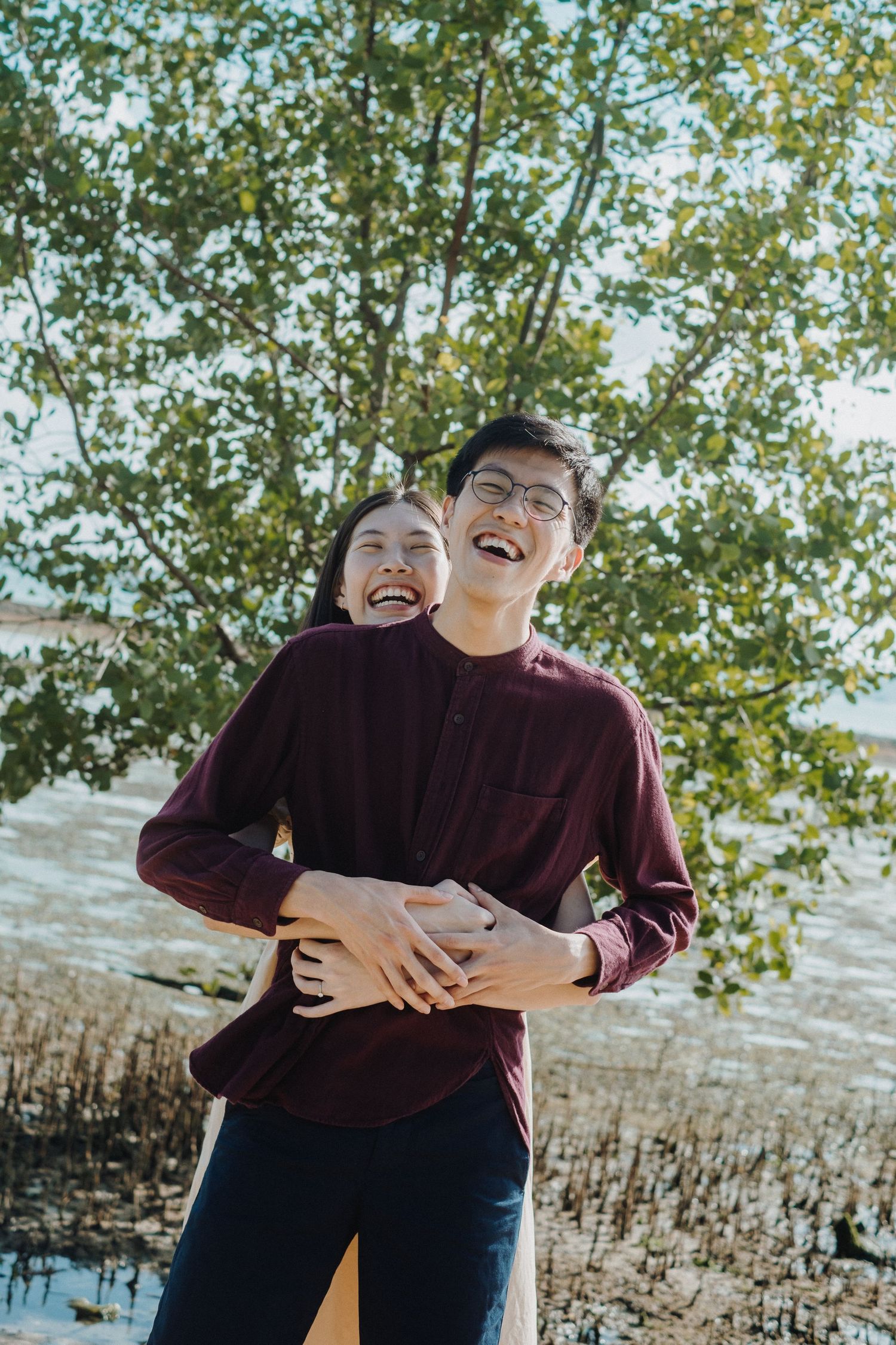 Two people sharing laughter and embracing outdoors against a leafy background.