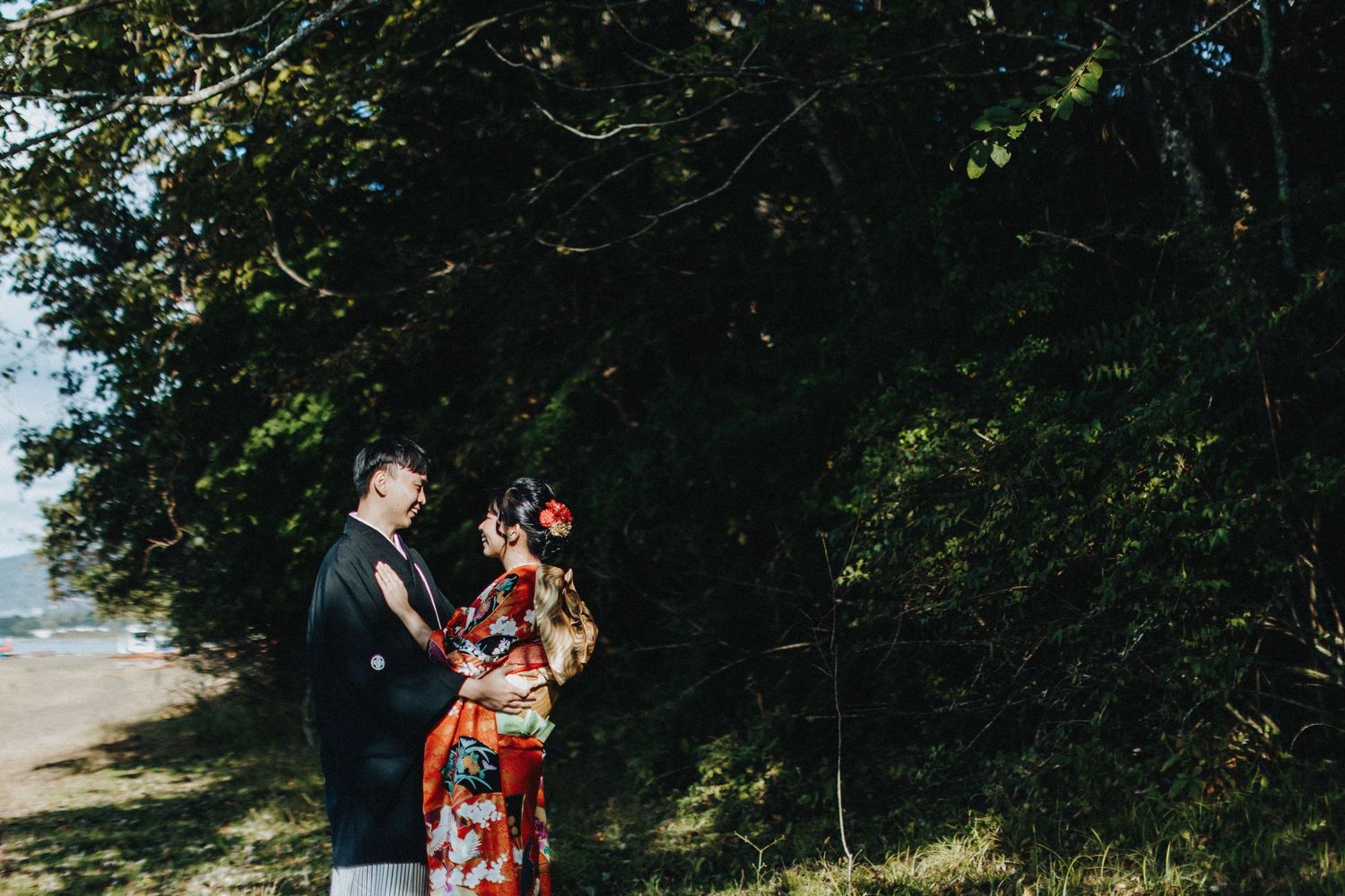 A couple strolls through a lush garden pathway wearing traditional Japanese kimono and formal western clothing.