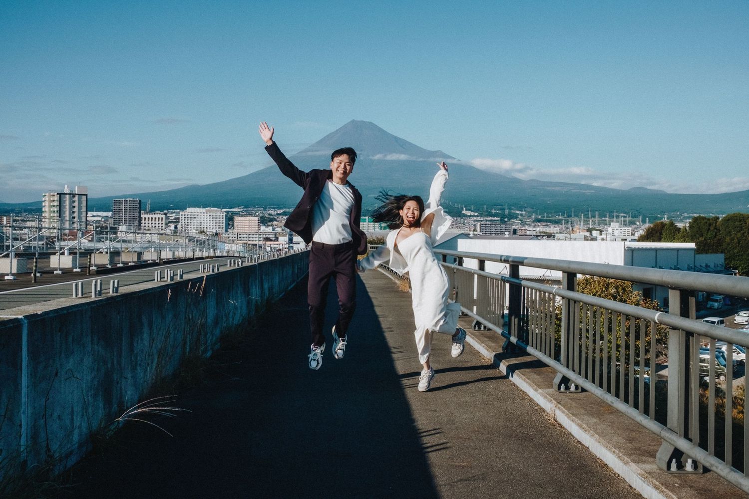 People pose joyfully on red bridge walkway with mountain vista in background.