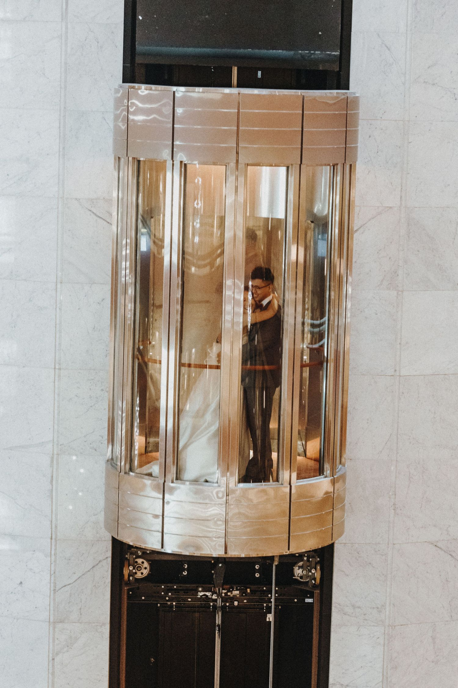 Modern glass elevator with reflective surfaces in an elegant building interior.