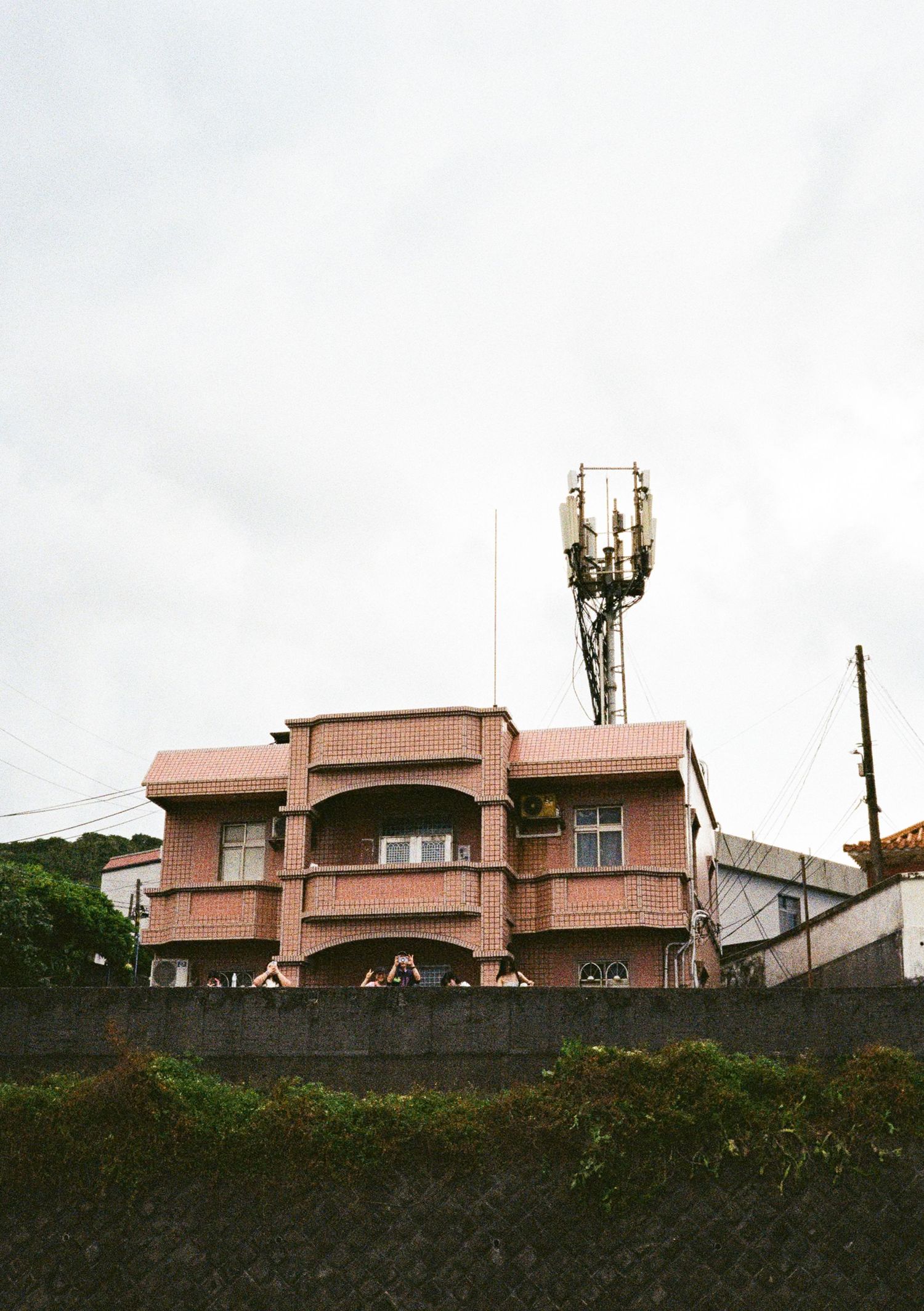 Pink-colored residential buildings with antennas visible on top of a dark stone retaining wall.