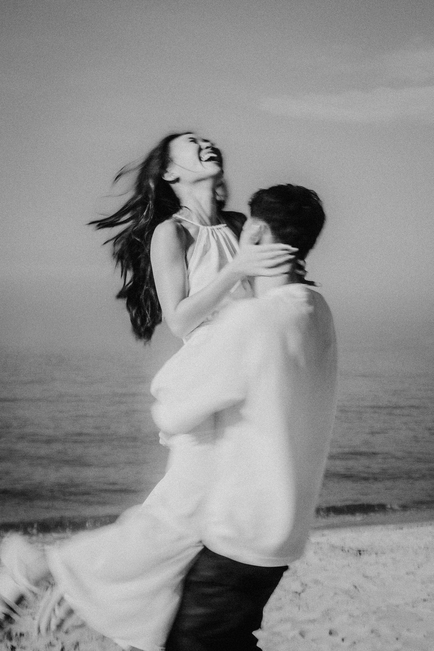 Couple embracing in white clothing on the beach in black and white photography.