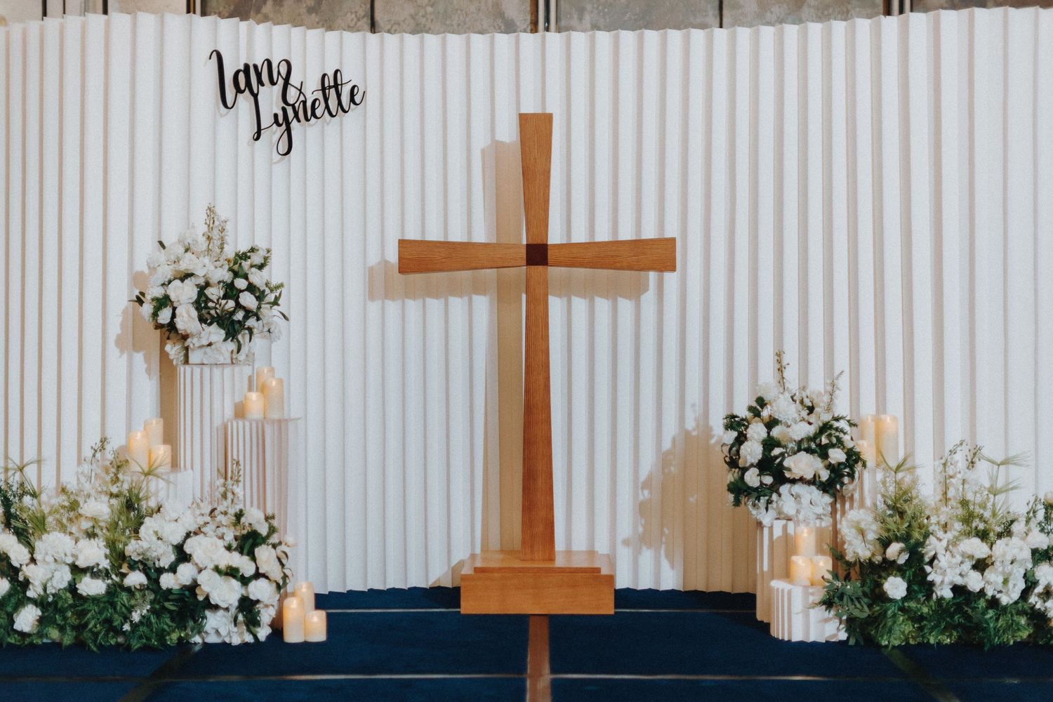 Modern wedding ceremony setup with wooden crosses and white floral arrangements.