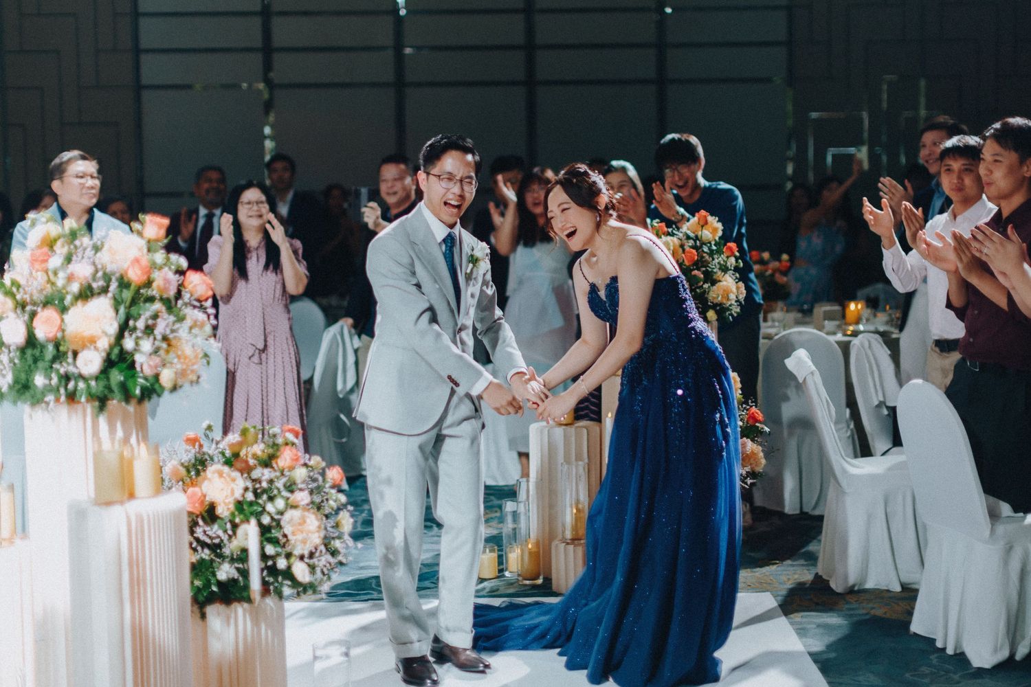 Wedding reception scene with elegant white decor, floral arrangements, and guests in formal attire.