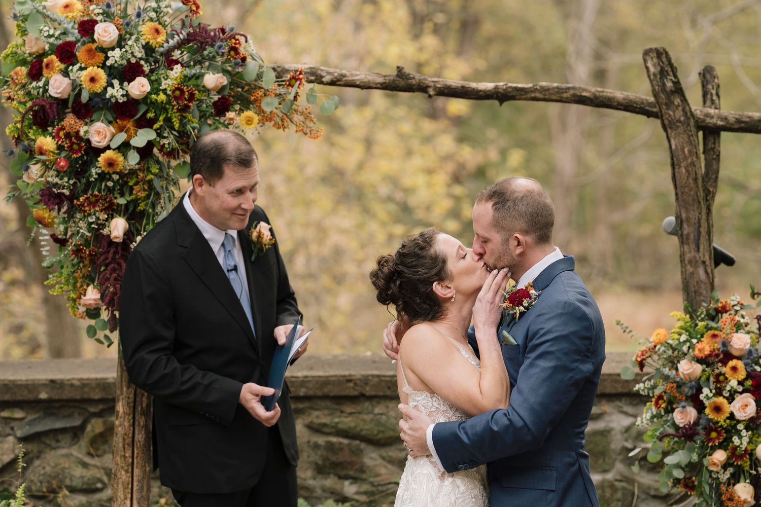 A husband and wife having their first kiss, with their officiant standing in the background