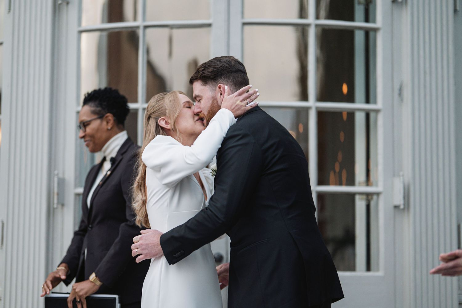 A husband and wife having their first kiss as the officiant gets out of their way