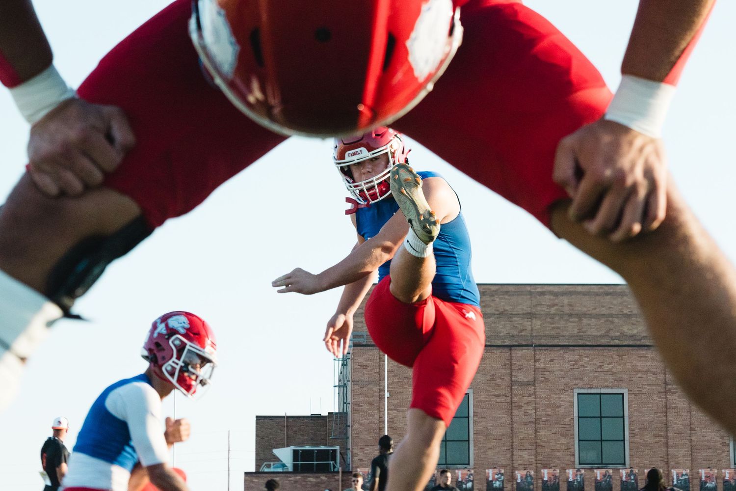 Football players in red and blue uniforms compete during a game with a low angle view through legs. photo bydaviel.com