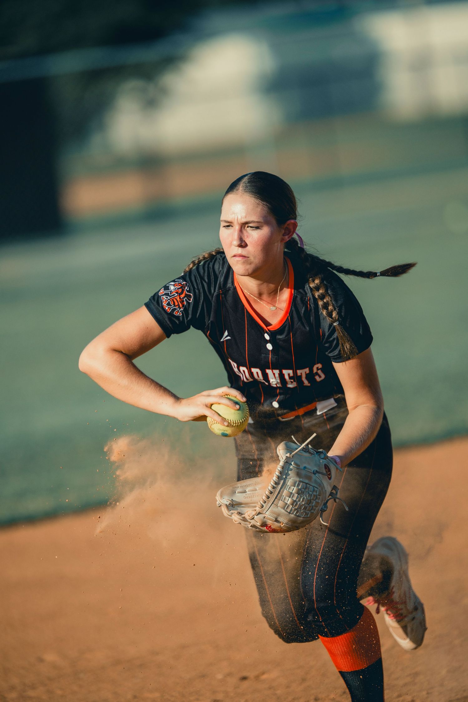 Softball player in black Hornets uniform preparing to throw on dirt field.