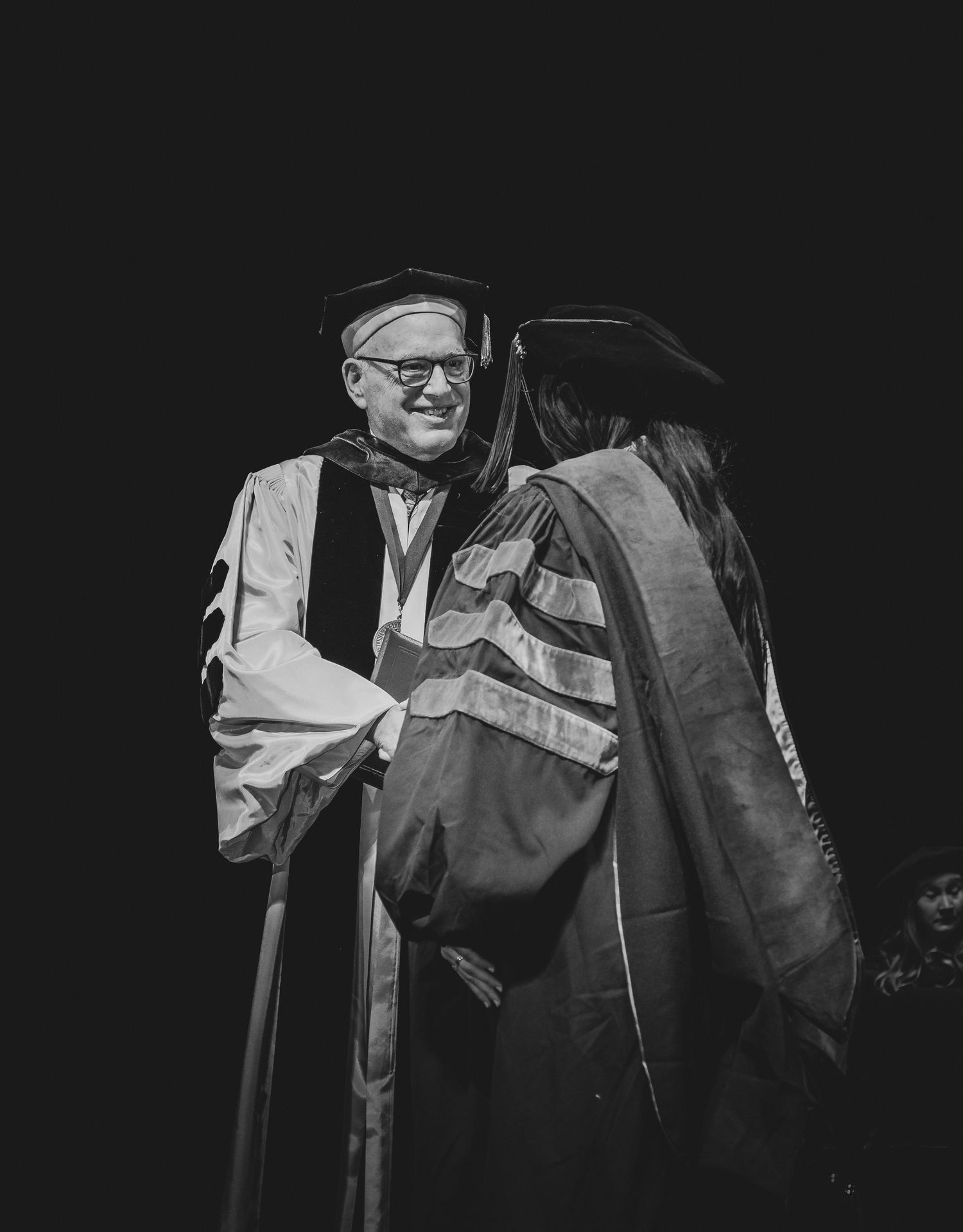 Black and white image of people in graduation robes during a ceremony.