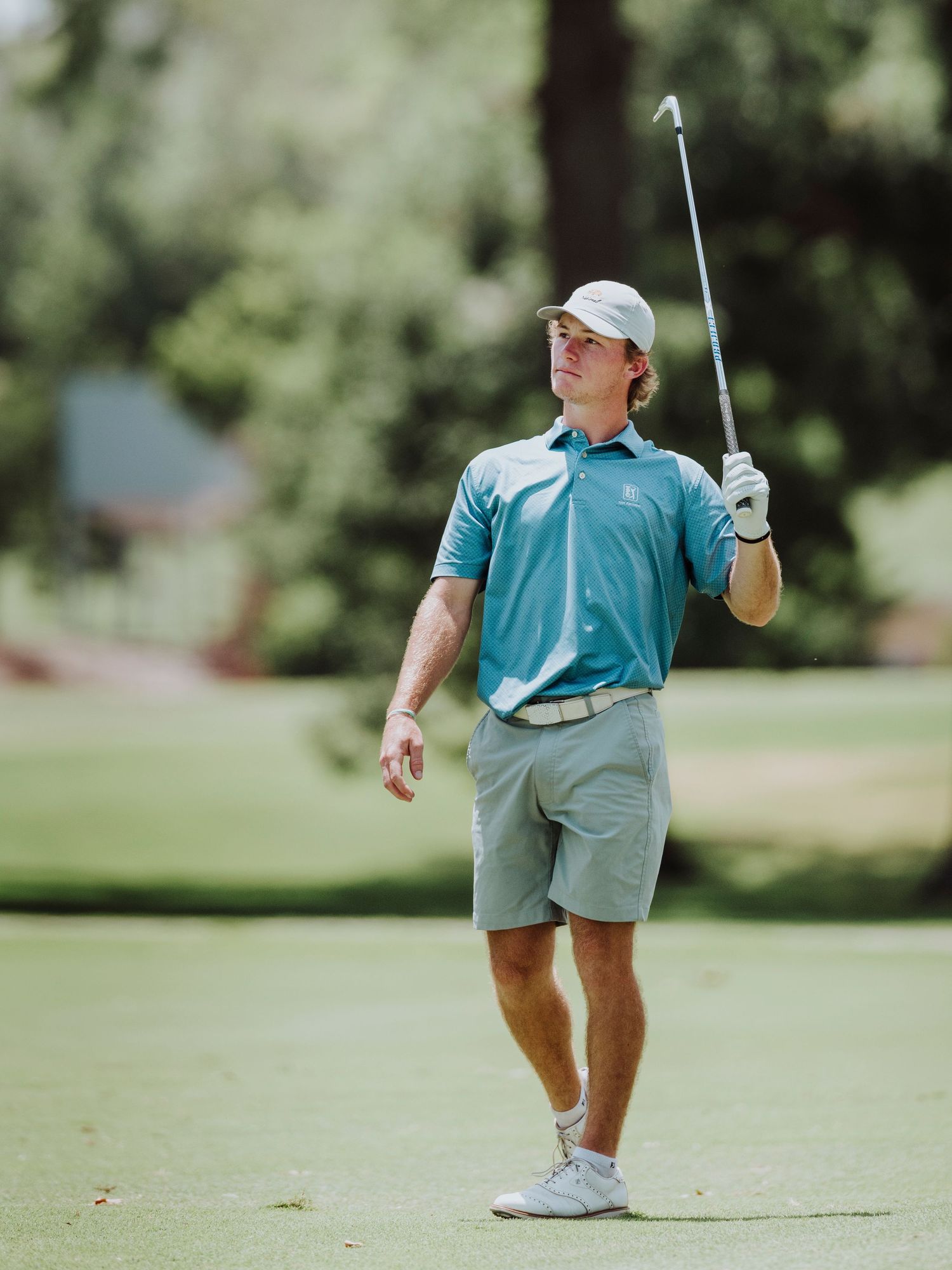 Golfer in light blue shirt practices putting stance on green grass course.
