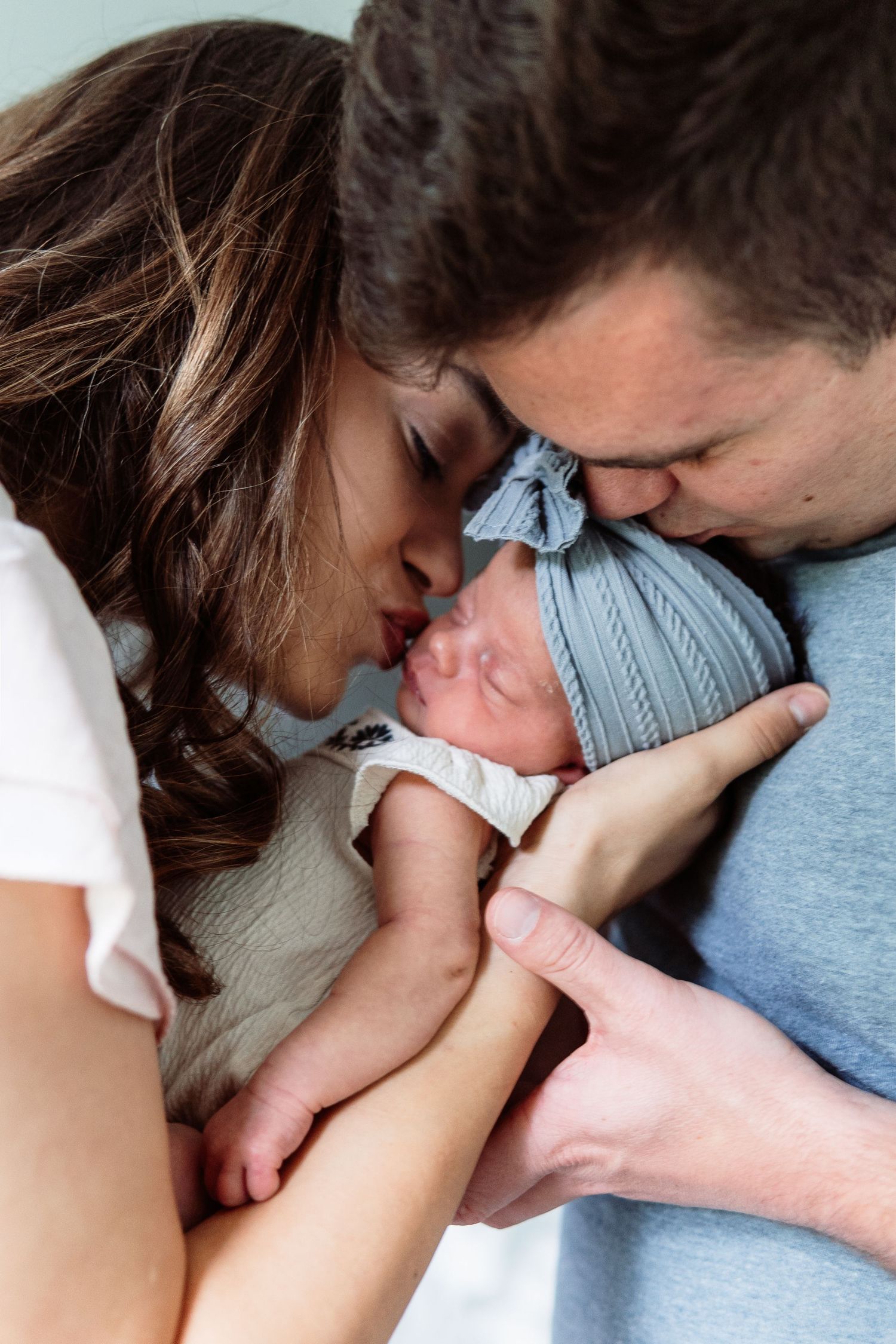 Intimate family moment as parents snuggle close to their newborn baby in soft lighting.