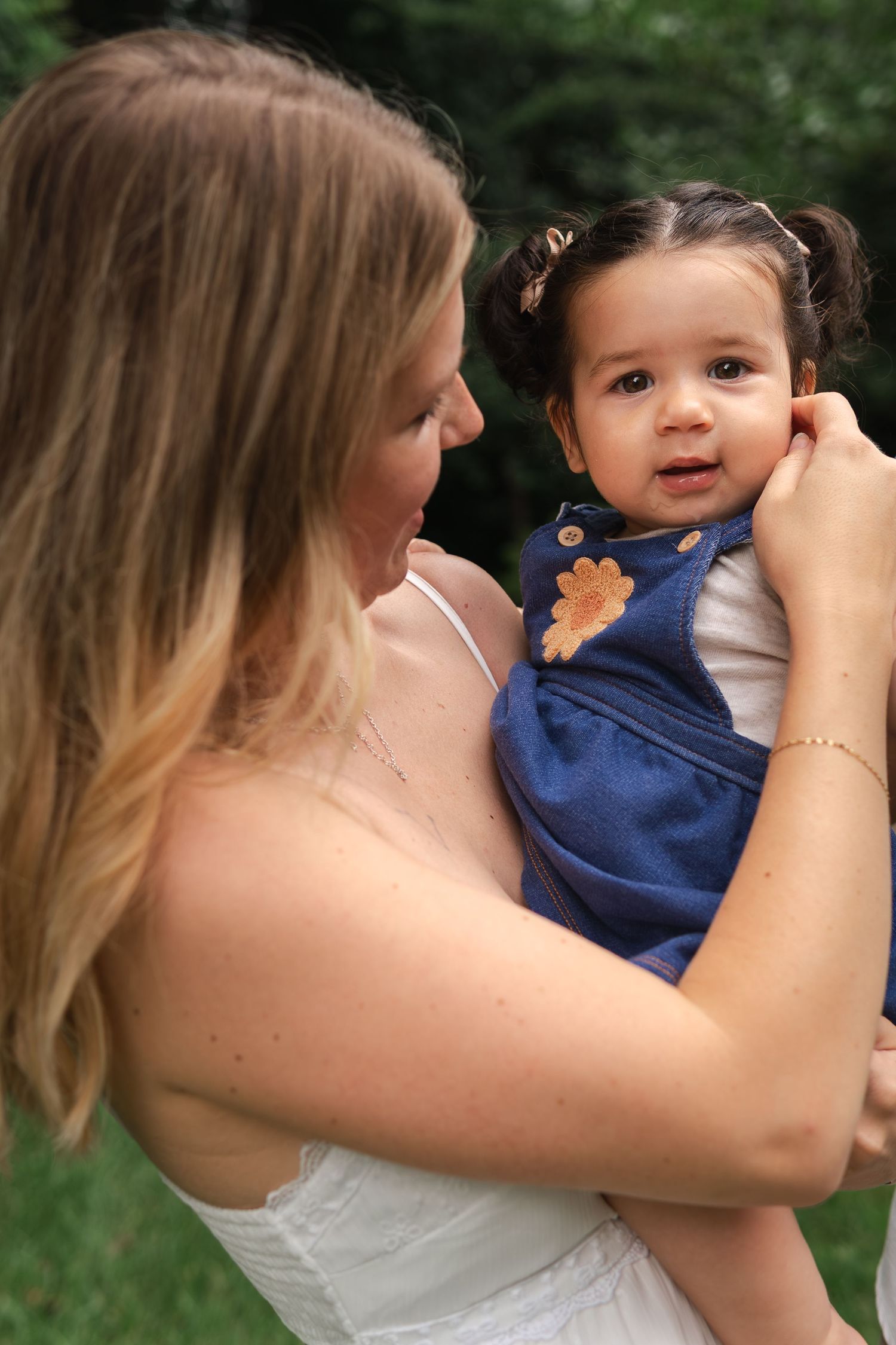 A tender moment captured outdoors as a woman in white holds a small child wearing a blue dress.