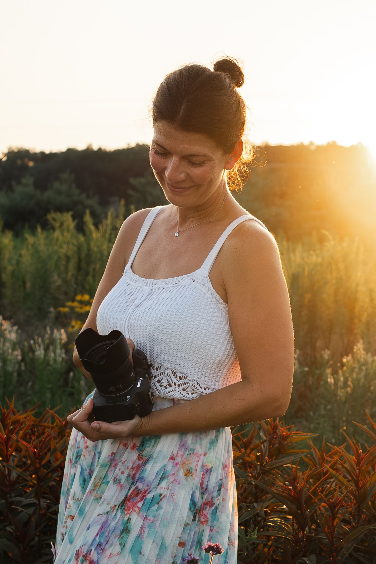 Person in white top and floral skirt holds black cat during golden hour sunset in field.