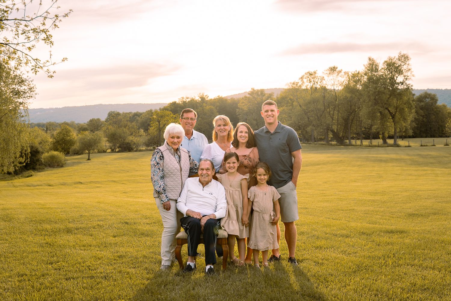 Family group poses together in a golden meadow at sunset during an outdoor portrait photography session.