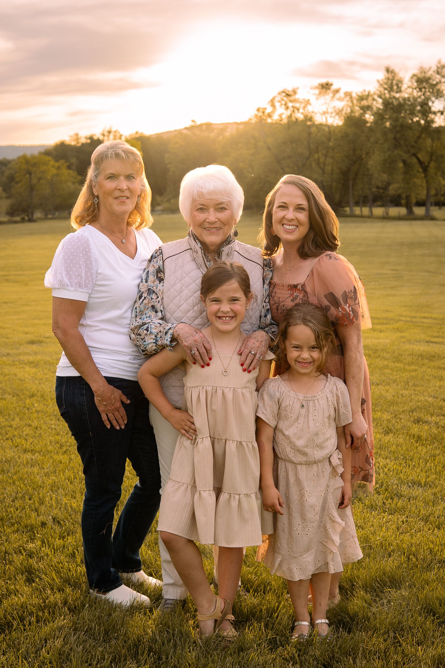 Family gathers for heartwarming outdoor portrait session in a sunlit field at dusk.