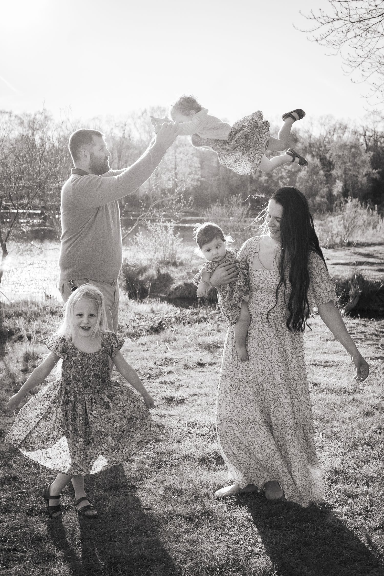 A family in floral dresses plays and dances together in a sunlit outdoor setting during golden hour in Haymarket, Virginia.