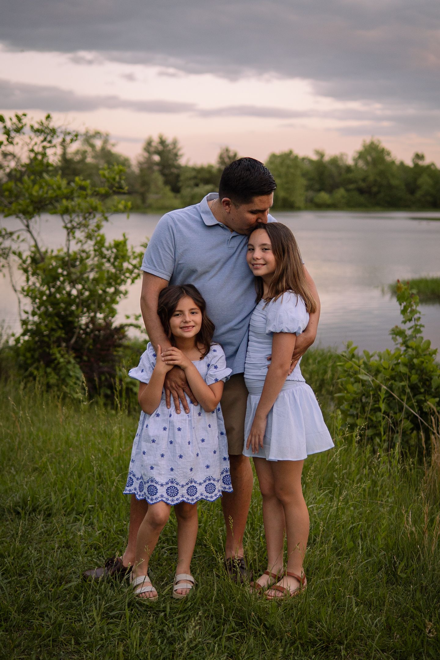 A heartwarming family moment beside a lake at sunset with coordinated blue and white outfits.