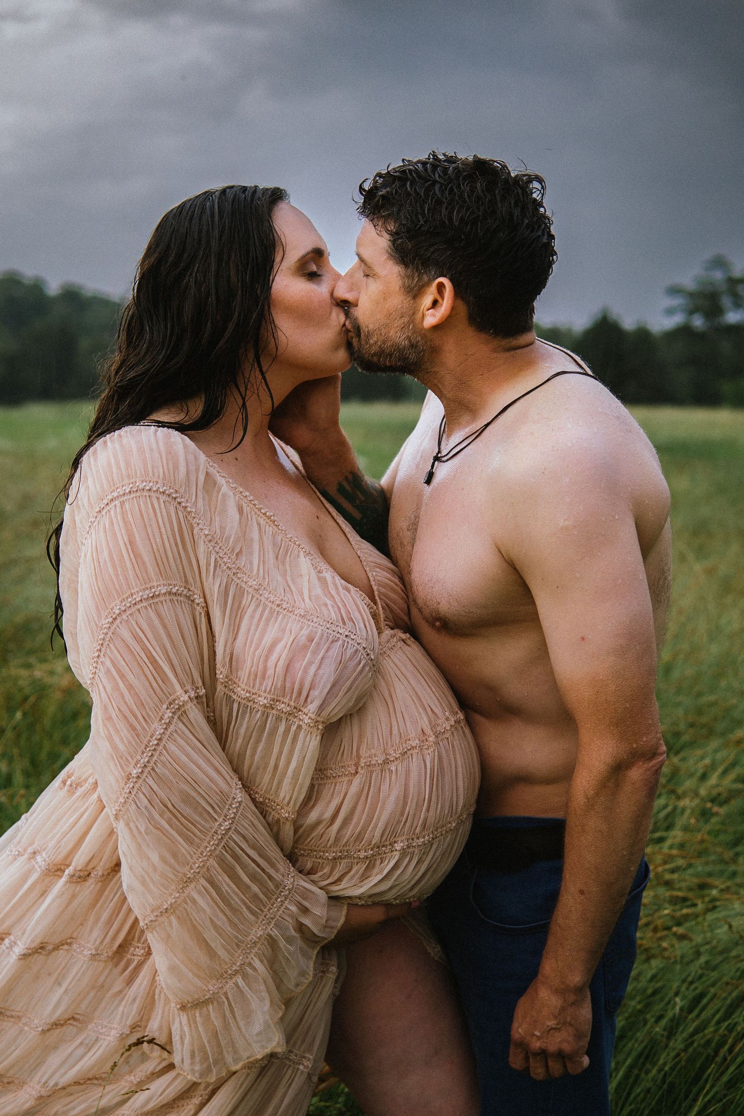 A romantic couple shares an intimate kiss while standing in a grassy field wearing casual attire.