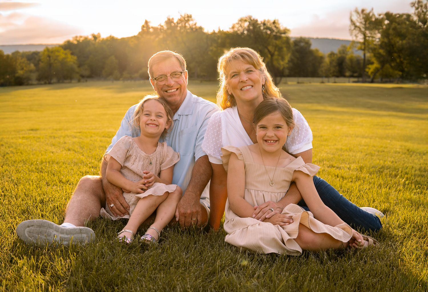 Family of four sitting together on grass during golden hour with mountains in background.