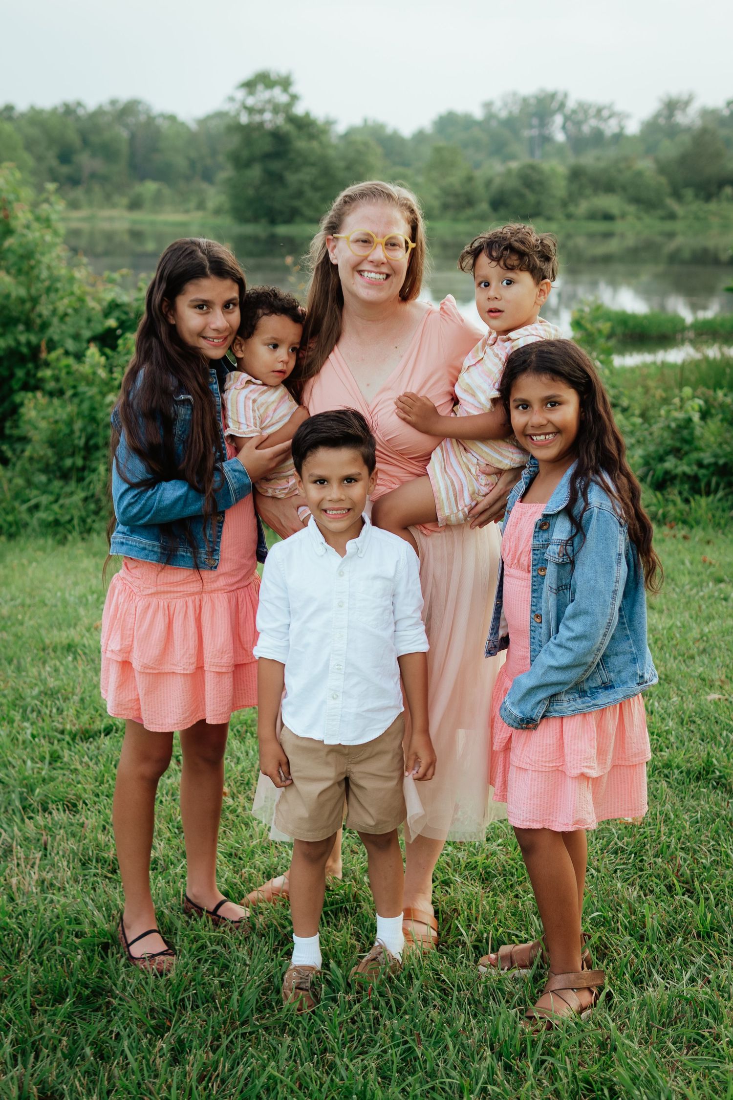 Family group photo at a lakeside park with coordinated pink and denim outfits.