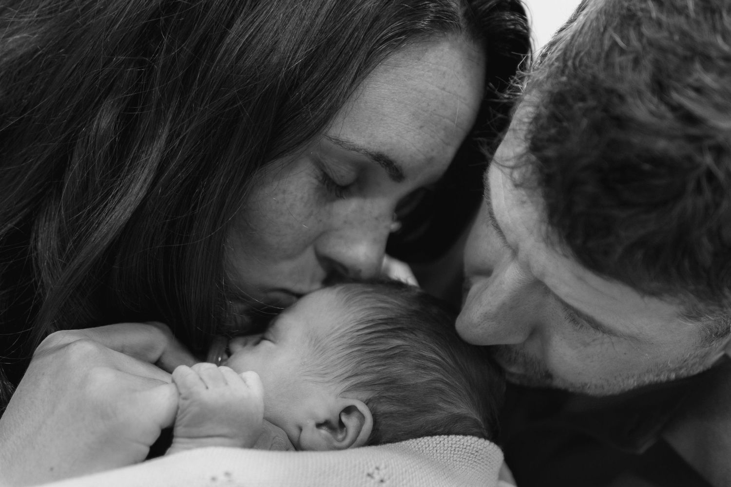 Tender black and white portrait of parents embracing their sleeping newborn.