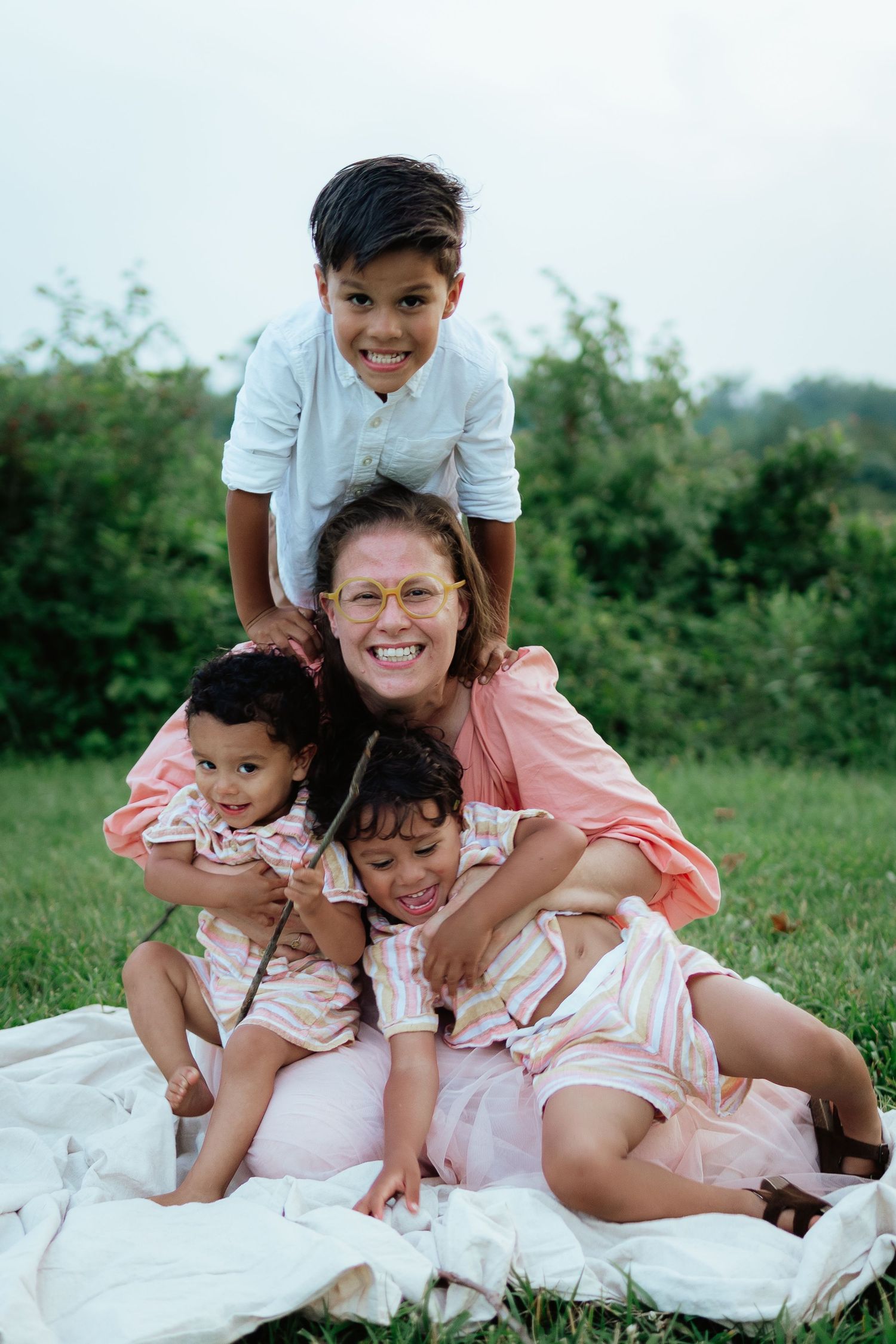A family group poses playfully on a white blanket in a grassy outdoor setting.