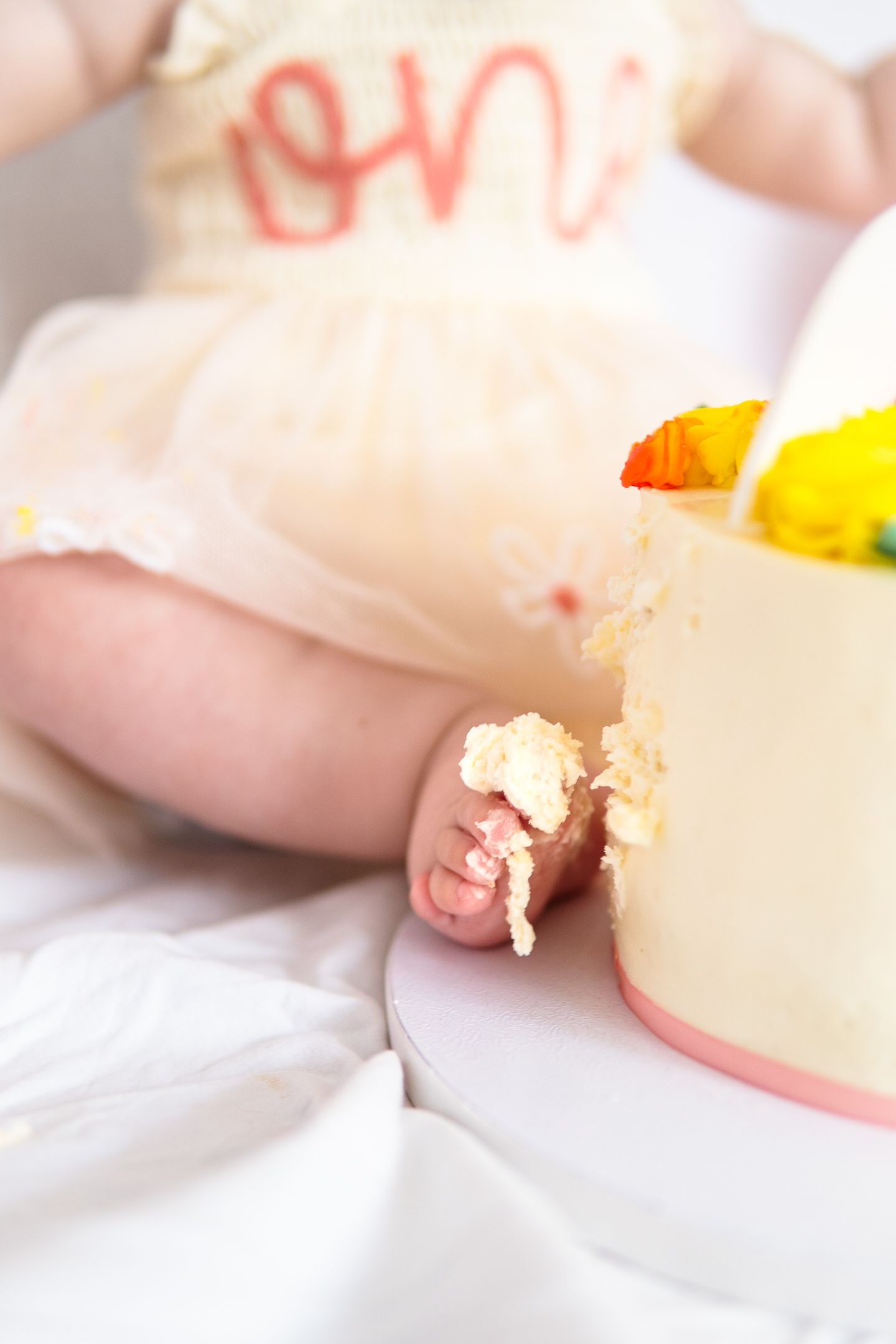 Close-up of tiny fingers touching frosting on a birthday cake.