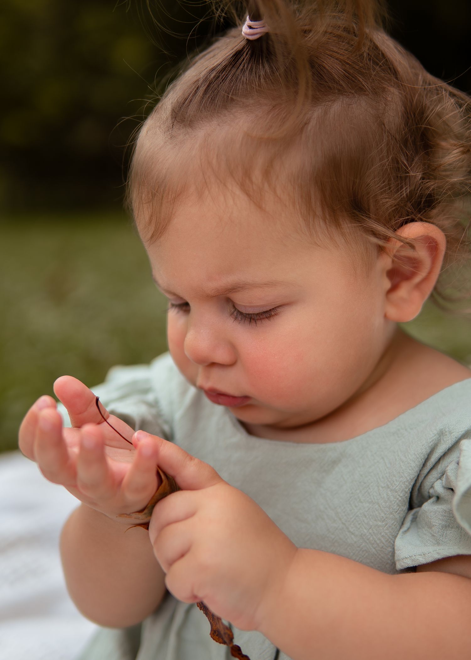A small child in a gray shirt carefully examines and holds a butterfly that has landed on their finger.